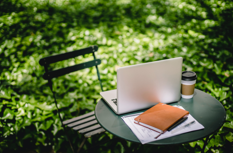 LemmenLearning visuele afbeelding: Een zilveren laptop en lichtbruine boek op een groene tafel in een natuur groene omgeving.
